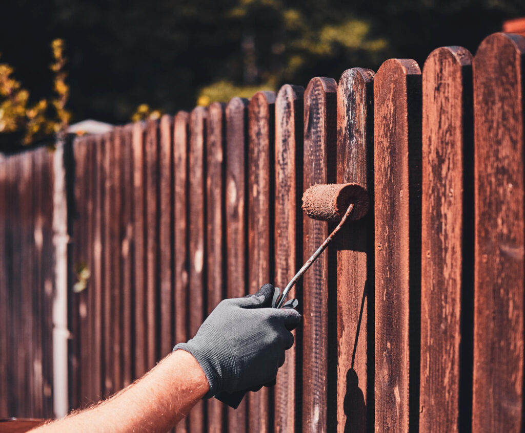 man-protective-gloves-is-painting-wooden-fence-bright-summer-day